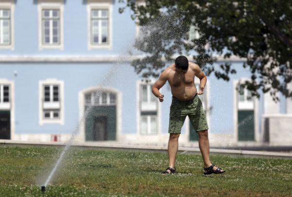 A man walks under the water from a garden sprinkler by the Tagus riverbank in Lisbon, Thursday, Aug. 2 2018. (AP Photo/Armando Franca)