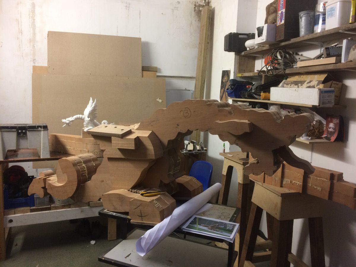 A kit-set dragon, with all the materials to make a dragon: a 3D-printed maquette (left), the rough dragon of 4-inch laminated strips of African cedarwood (center), and rolled up are full-scale blueprints for the dragon. (Sands & Randall)