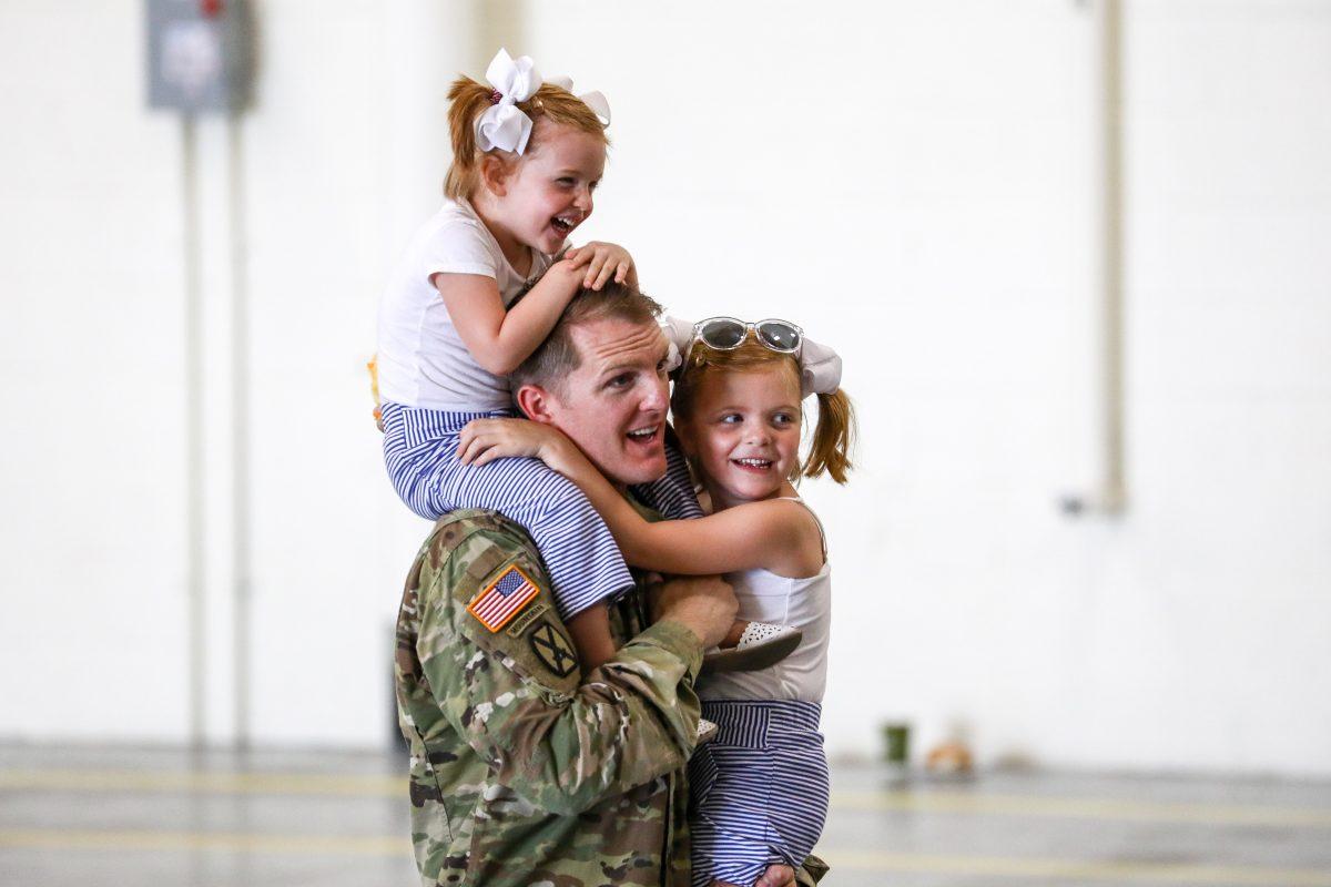A soldier from the 10th Mountain Division carries his daughters before an event in which President Donald Trump signed the 2019 National Defense Authorization Act at Wheeler-Sack Army Airfield, at Fort Drum, N.Y., on Aug. 13, 2018. (Charlotte Cuthbertson/The Epoch Times)