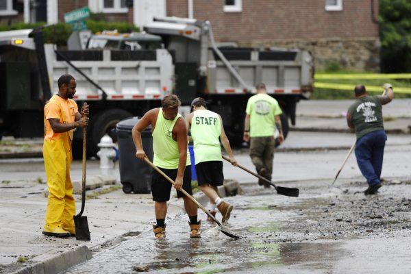 Workers clean up debris swept into the street during flooding in Upper Darby, Pa., Monday, Aug. 13, 2018. (AP Photo/Matt Rourke)