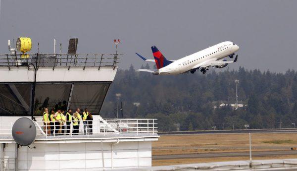 People stand at the ramp tower, used to control airplane traffic, as a plane takes off behind them at Seattle-Tacoma International Airport Monday, Aug. 13, 2018, in SeaTac, Wash. A turboprop plane was stolen from the airport by an airline ground agent on Friday, and later crashed into a small island in the Puget Sound, killing the man. (AP Photo/Elaine Thompson)