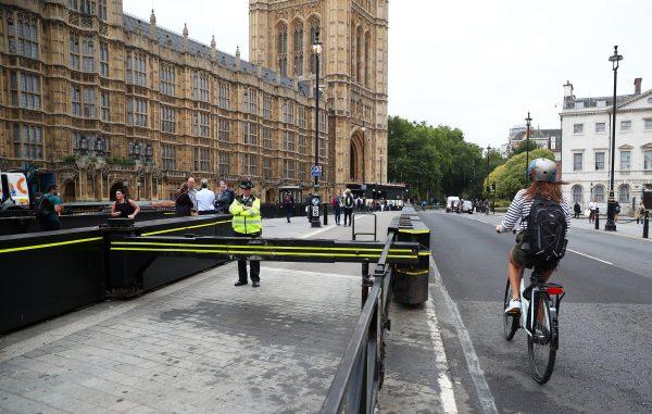 A cyclist passes a police officer standing at the vehicle barrier to the Houses of Parliament where a car crashed after knocking down cyclists and pedestrians yesterday in Westminster, London on Aug. 15, 2018. (Reuters/Hannah McKay)
