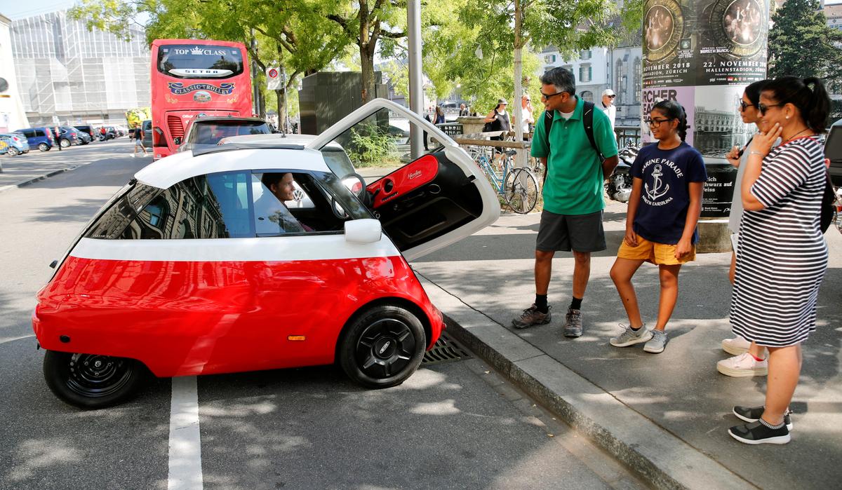 Chief Marketing Officer Merlin Ouboter (L) of Swiss Microlino AG sits in an electric-powered Microlino car as he answers questions of tourists from the United States in Zurich, Switzerland Aug. 16, 2018. (Reuters/Arnd Wiegmann)