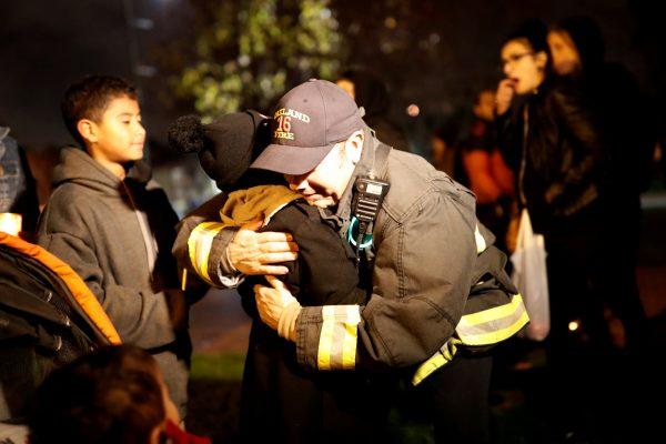 A firefighter embraces a child during a vigil for the victims of the fatal warehouse fire in Oakland, Calif., Dec. 5, 2016. (Reuters/Stephen Lam)