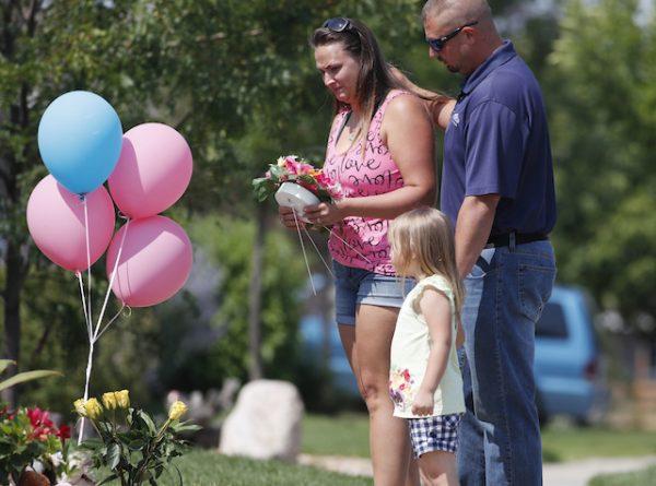 Ashley Bell, left, is consoled by her husband, Steven, and 4-year-old daughter Liberty as the woman places a tribute outside the home where a pregnant woman and her two daughters lived on Aug. 16, 2018, in Frederick, Colo. (AP Photo/David Zalubowski)