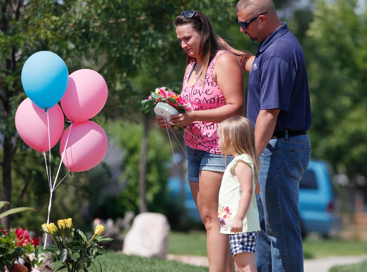 Ashley Bell, left, is consoled by her husband, Steven, and 4-year-old daughter Liberty as the woman places a tribute outside the home where a pregnant woman and her two daughters lived in Frederick, Colorado on Aug. 16, 2018. (AP Photo/David Zalubowski)