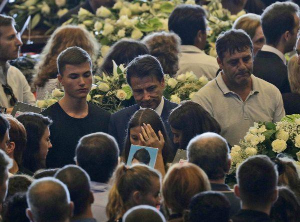 Italian Premier Giuseppe Conte, center, walks past relatives of some of the victims of a collapsed highway bridge at the end of their funeral service, in Genoa's exhibition center Fiera di Genova, Italy, Aug. 18, 2018. (AP/Gregorio Borgia)