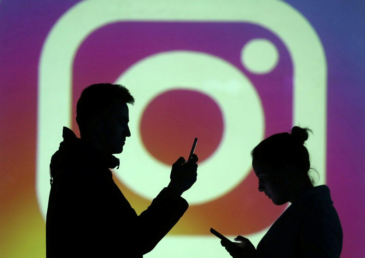 Silhouettes of mobile users are seen next to a screen projection of Instagram logo in this picture illustration taken March 28, 2018. (Dado Ruvic/Illustration/Reuters)
