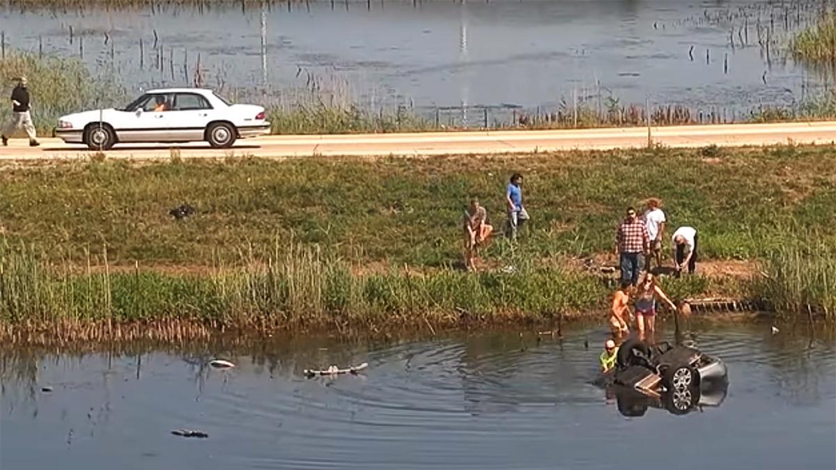 Bystanders flock to the scene where a woman’s car flipped and slid into a retention pond. (Illinois State Police via Storyful screenshot)