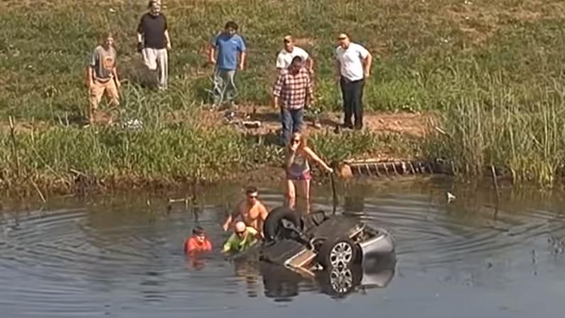 Two men pull the still-submerged victim out of the upside-down car. (Illinois State Police via Storyful screenshot)