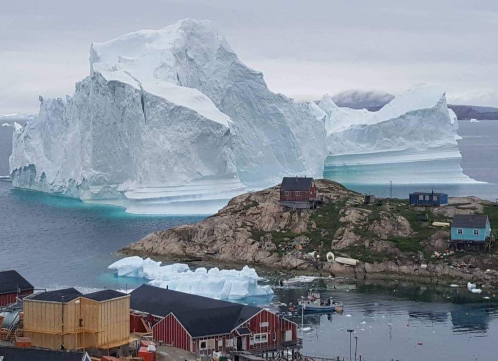 An iceberg behind houses and buildings outside the village of Innarsuit, an island settlement in the Avannaata municipality in northwestern Greenland. (Magnus Kristensen/AFP/Getty Images)