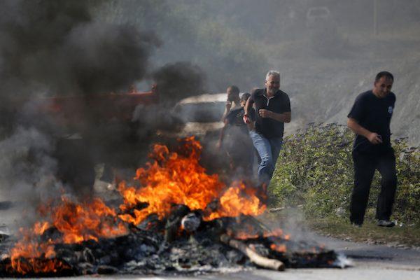 Kosovo Albanians run past a fire burning at a roadblock in Vojtesh, Kosovo, on Sept. 9, 2018. (AP Photo/Visar Kryeziu)