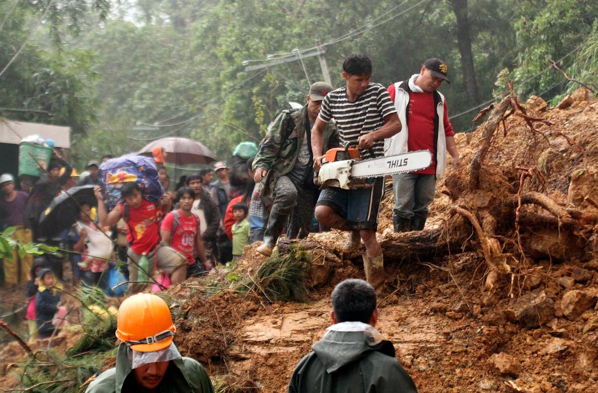 Residents and relatives of miners in Itogon township, Benguet province in the northern Philippines wait as a worker cuts a toppled tree with a chainsaw as they evacuate following landslides triggered by Typhoon Mangkhut burying an unknown number of miners and isolating the township. Typhoon Mangkhut barreled into southern China on Sept. 16, 2018, after lashing the northern Philippines with strong winds and heavy rain that left more than dozens dead from landslides and drownings. (By Jayjay Landingin/AP Photo)