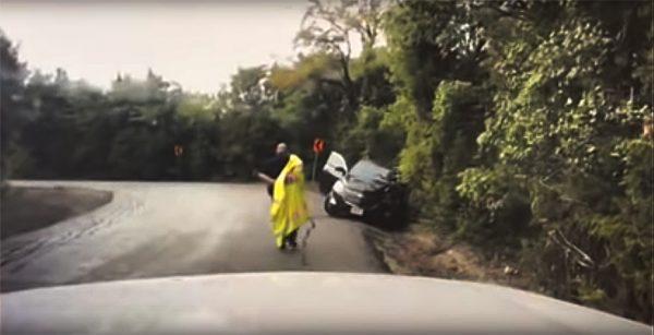 Officer Blair takes off his raincoat as he approaches the stranded motorist, seeing that she has no protection from the rain. (Screenshot/Anna Police Department)