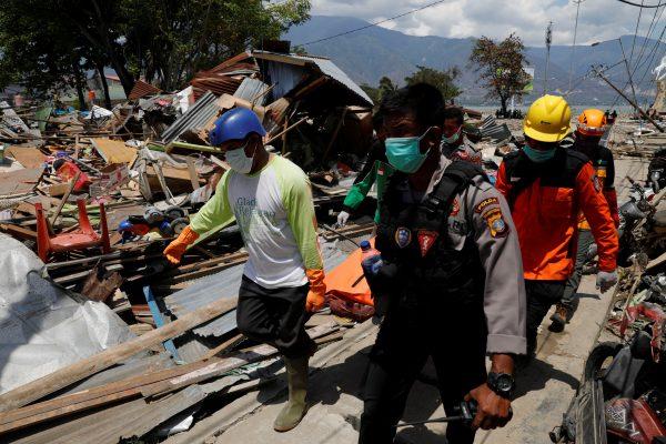 Rescue team members carry a dead body as they walk among ruins after the earthquake in Palu, in Indonesia's Sulawesi Island, Oct. 2, 2018. (Reuters/Beawiharta)