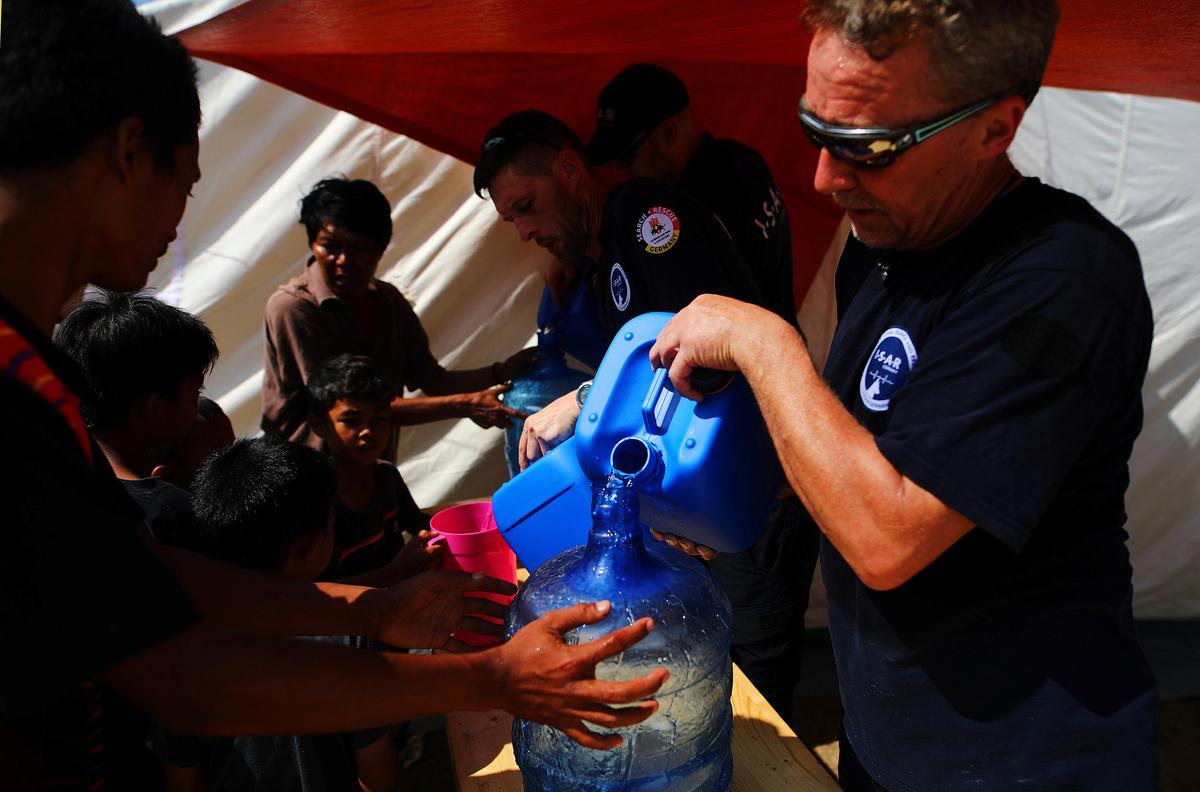 Members of Germany's NGO organisation ISAR-Germany (International Search and Rescue) give purified water to people at a suburb of Palu, Central Sulawesi, Indonesia, October 9, 2018. (Hannibal Hanschke/Reuters)