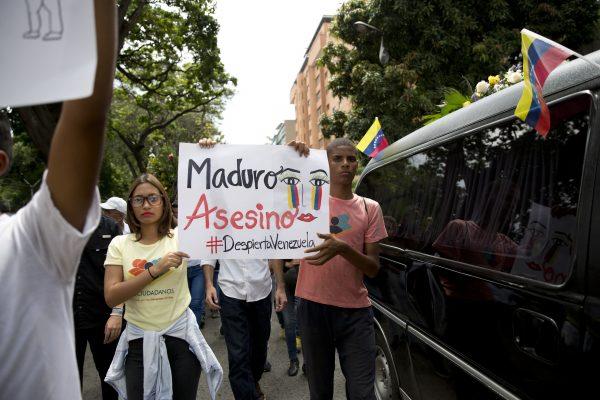 People hold up a sign that in Spanish reads "Maduro Assassin" as they walk next the hearse holding the remains of opposition activist Fernando Alban, during his funeral in Caracas, Venezuela, on Oct. 10, 2018. (Ariana Cubillos/AP)