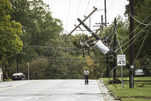 A pedestrian walks under downed power lines due to Michael, on Cherry Street, south of Polo Road, in Winston-Salem, N.C., on Oct. 11, 2018. (Andrew Dye/The Winston-Salem Journal/AP)