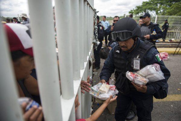 A Mexican federal police officer hands out food to Honduran migrants stuck in no man's land on the bridge over the Suchiate River that is the border between Guatemala and Mexico, near Ciudad Hidalgo, Mexico, on Oct. 20, 2018. (Oliver de Ros/AP Photo)