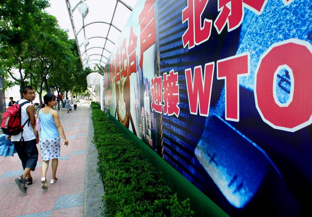 A young Chinese couple walk by a billboard promoting China's membership to the World Trade Organization (WTO), along a street in Beijing on July 17, 2001. (Goh Chai Hin/AFP/Getty Images)