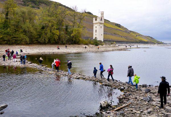 People walk over stones looking out of the river Rhine to the Maeuseturm (mice tower) of Bingen, Germany, which usually sits on an island, on Oct.24, 2018. (AP Photo/Michael Probst)