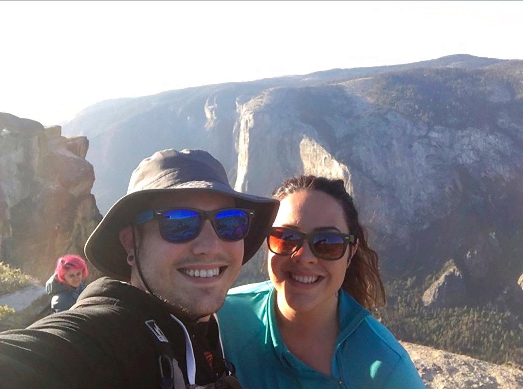 Sean Matteson poses for a selfie with his girlfriend Drea Rose Laguillo, in Yosemite National Park, California on Oct. 21, 2018. The couple said Meenakshi Moorthy, seen in background at left, the pink-haired woman who fell to her death in Yosemite Park accidentally appeared in two of their selfie photos taken shortly before the 30-year-old old fell from a popular overlook. (Sean Matteson via AP)