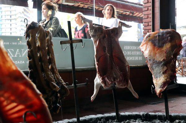 People walk by a barbecue restaurant as pieces of beef and pork are being cooked in Buenos Aires, Argentina on Oct. 18, 2018. (Marcos Brindicci/Reuters)