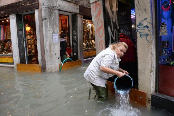 A woman removes water from a shop in a flooded street of Venice, Italy, on Monday, Oct. 29, 2018. (Andrea Merola/ANSA via AP)