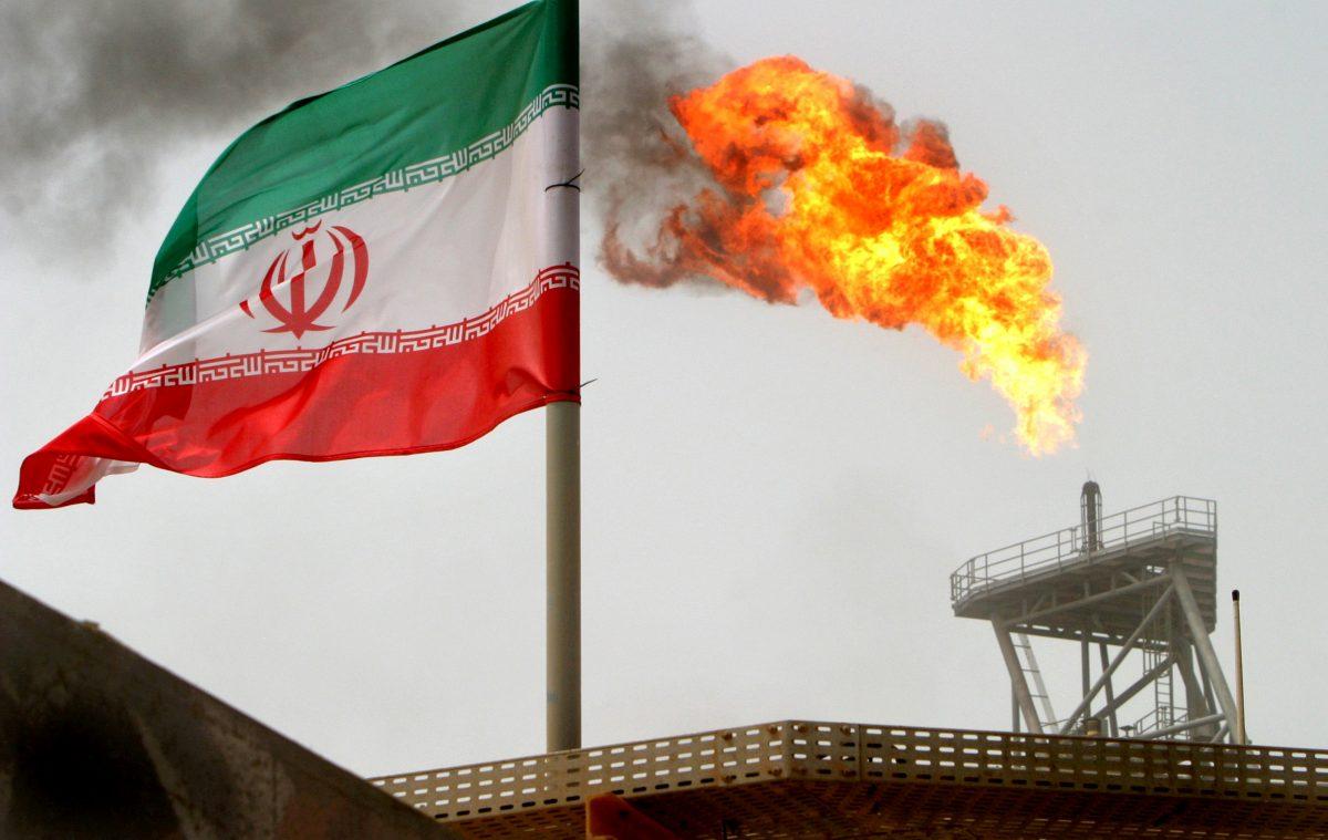 A gas flare on an oil production platform in the Soroush oil fields is seen alongside an Iranian flag in the Persian Gulf, Iran, on July 25, 2005. (Reuters/Raheb Homavandi/File Photo