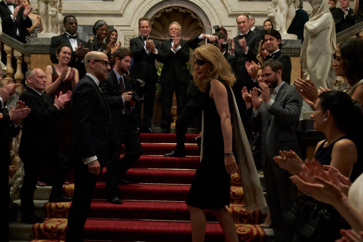 Marie Colvin (Rosamund Pike, foreground, C) is applauded as she enters the British Press Awards with boyfriend Tony Shaw (Stanley Tucci, foreground, L) in “A Private War.” (Paul Conroy/Aviron Pictures)