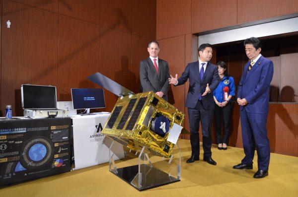 Astroscale CEO Nobu Okada (C) demonstrates a mockup of his company’s space debris removal apparatus to Japanese Prime Minister Shinzo Abe (R) on March 20, 2018. (Courtesy of Astroscale)