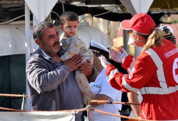 A member of the Red Cross welcomes a man holding a child as they disembark from rescue ship Aquarius on October 13, 2017 in Palermo, Sicily. (Alessandro Fucarini/AFP/Getty Images)