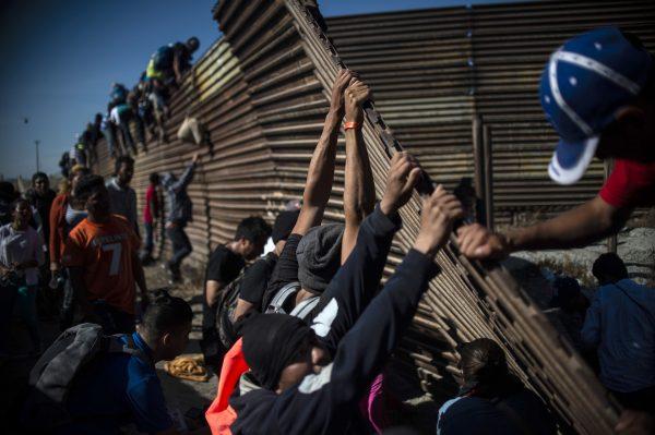 A group of Central American migrants climb the border fence between Mexico and the United States as others try to bring it down, near El Chaparral border crossing, in Tijuana, Baja California State, Mexico, on Nov. 25, 2018. (Pedro Pardo/AFP/Getty Images)