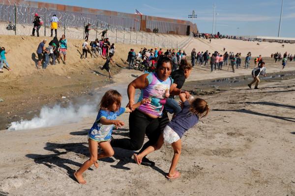 A migrant family, part of a caravan of thousands traveling from Central America en route to the United States, run away from tear gas in front of the border wall between the U.S. and Mexico in Tijuana. (Reuters)