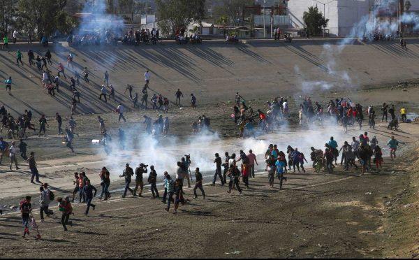 Migrants run from tear gas, thrown by the U.S. border patrol, near the border fence between Mexico and the United States in Tijuana, Mexico, Nov. 25, 2018. (Hannah McKay/Reuters)