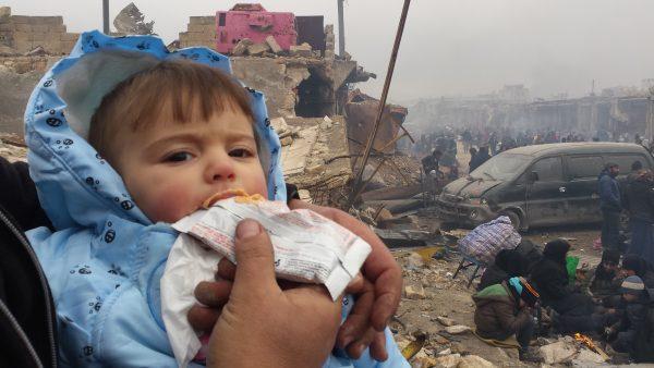 Abdulkafi Alhamdo holds his daughter, with the destruction of Aleppo in the background. (Courtesy of Abdulkafi Alhamdo)