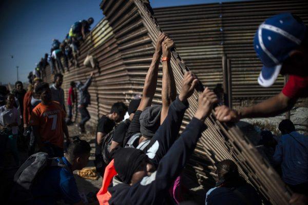 A group of Central American migrants climb the border fence between Mexico and the United States as others try to bring it down, near the El Chaparral border crossing, in Tijuana, Baja California State, Mexico, on Nov. 25, 2018. (Pedro Pardo/AFP/Getty Images)