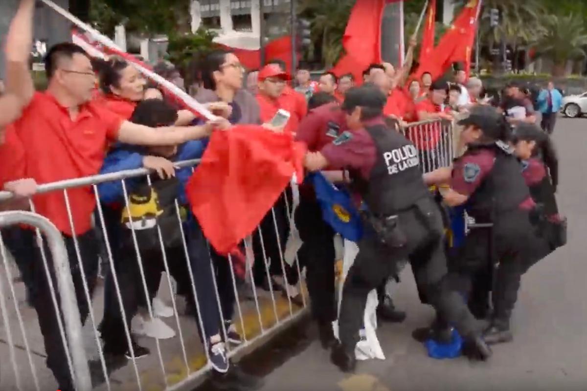A male participant in a pro-Beijing group (L) jabs at a Falun Gong practitioner with a flagpole as police officers attempt to pull away the practitioner's banner, in Buenos Aires, Argentina, ahead of the G-20 summit. (Screenshot via YouTube)