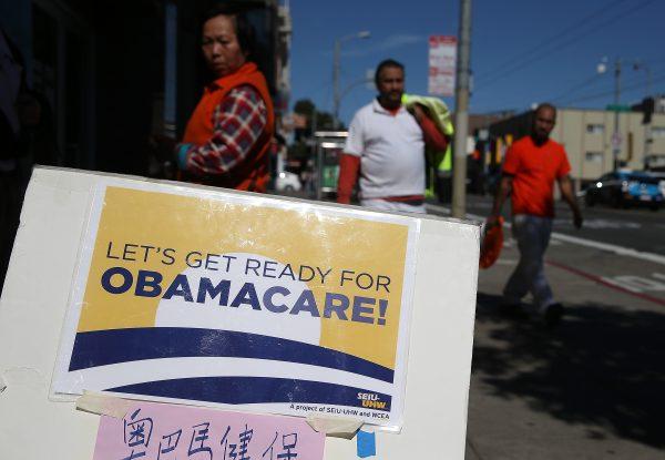 Pedestrians walk by a sign posted outside of a health care enrollment fair in San Francisco, Calif., on March 18, 2014. (Photo by Justin Sullivan/Getty Images)
