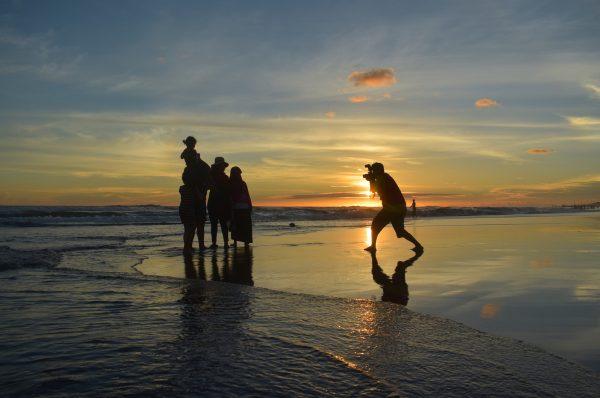 A photographer takes a picture of a family on a beach. (Pixabay)