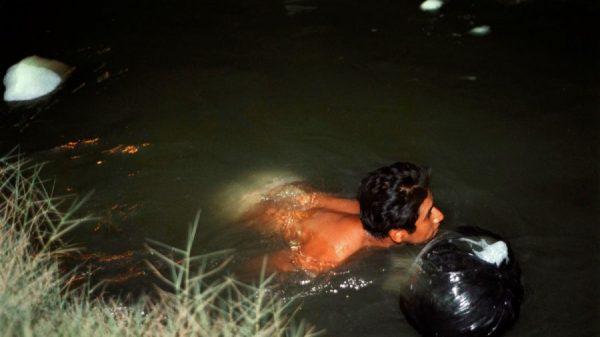 A man swims with a garbage bag containing dry clothing down the New River in a nighttime attempt to elude United States Border Patrol agents while illegally crossing into the United States near Calexico, California in a March 18, 2000 file photo. An alien drowned in the nearby All-American Canal on Dec. 5, 2018, Border Patrol agents said. (Photo by David McNew/Online USA)