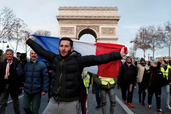 A protester holds the French flag as he walks with others wearing yellow vests who take part in a demonstration by the "yellow vests" movement on the Champs Elysees below the Arc de Triomphe in Paris, France, Dec. 8, 2018. (Reuters/Benoit Tessier)