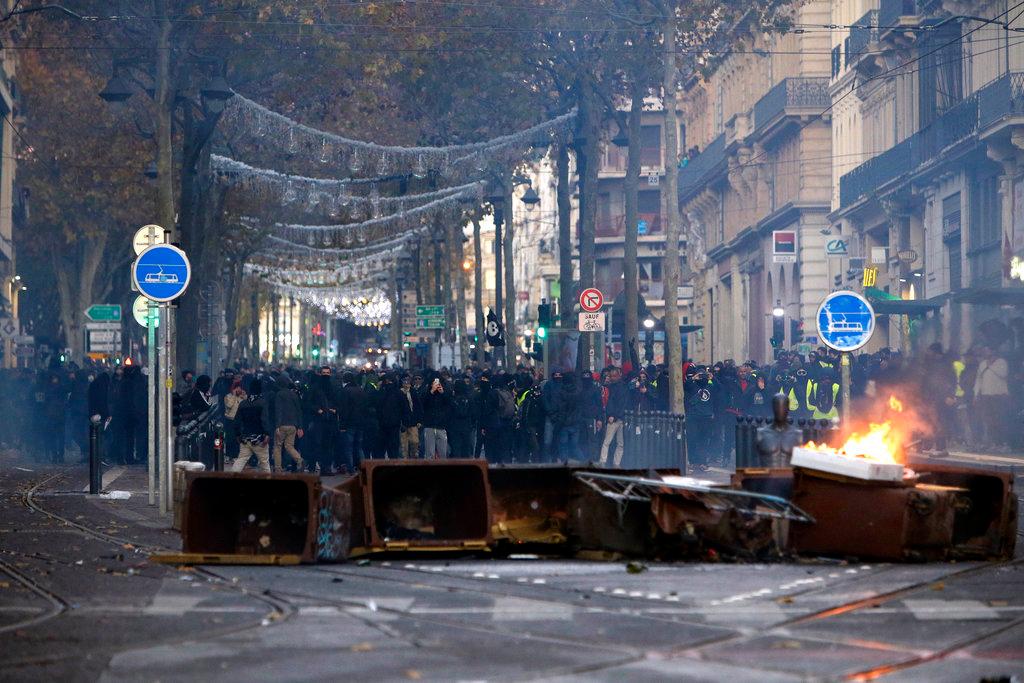 Demonstrators stand behind a burning bin during clashes, Saturday, Dec. 8, 2018 in Marseille, southern France. (AP Photo/Claude Paris)