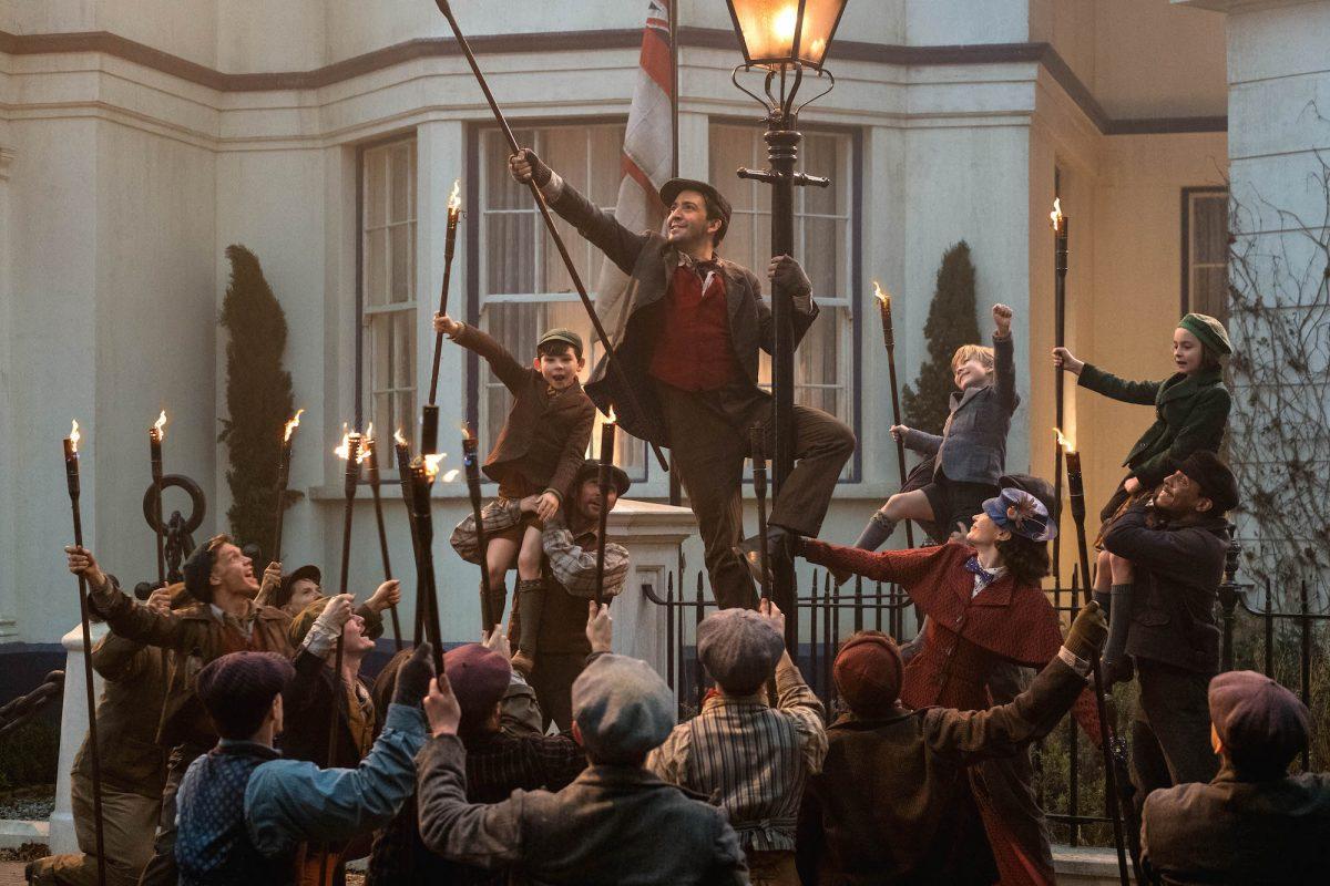 (L-R) Jack (Lin-Manuel Miranda), Mary Poppins (Emily Blunt), and the Banks children with a crew of street lamplighters at 17 Cherry Tree Lane in Disney's musical “Mary Poppins Returns.” (Disney)