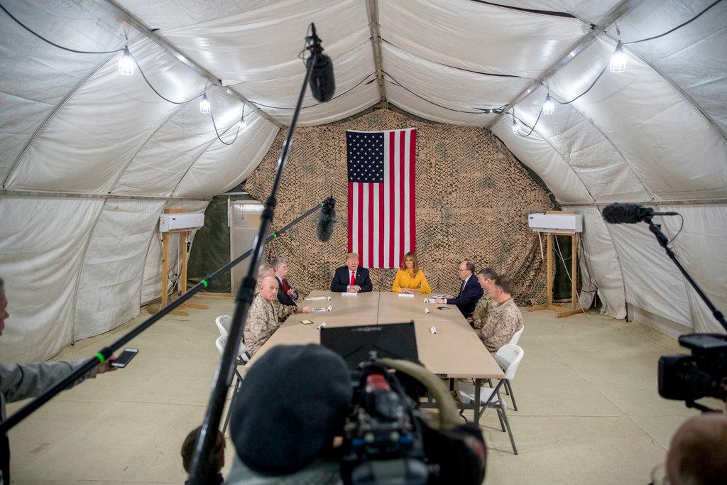 President Donald Trump, accompanied by national security adviser John Bolton, third from left, first lady Melania Trump, fourth from right, U.S. Ambassador to Iraq Doug Silliman, third from right, and senior military leadership, speaks to members of the media at Al Asad Air Base, Iraq, on Dec. 26, 2018. (AP Photo/Andrew Harnik)
