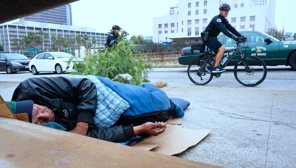 Los Angeles Police Department officers patrol on bicycles past a homeless man at his encampment on a downtown sidewalk in Los Angeles, Calif. on June 7, 2017 (Frederic Brown/AFP/Getty Images)