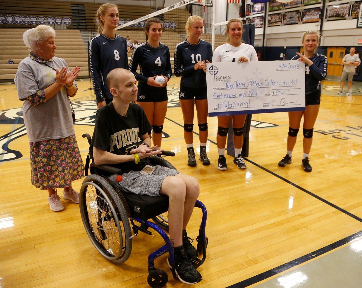 In this Sept. 4, 2018, photo, Central Catholic players present Tyler Trent, foreground, with a check to benefit Riley Children's Hospital before meeting Lafayette Jeff in a high school volleyball game, in Lafayette, Ind. (John Terhune/Journal & Courier via AP)