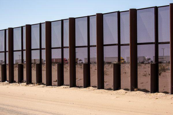 A line of trucks awaits inspection by the Mexican military in Mexico can be seen through the border fence on the U.S.–Mexico border near Yuma, Ariz., on May 25, 2018. (Samira Bouaou/The Epoch Times)