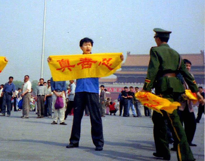 Chinese policeman approaches to arrest Falun Gong practitioners who traveled across China to Tiananmen Square, Beijing, to stage peaceful appeals against the persecution in 2001. The Chinese characters on the banner read "Zhen, Shan, Ren," the core moral teachings of the spiritual discipline. (Courtesy of <a href="http://en.minghui.org/">Minghui</a>)