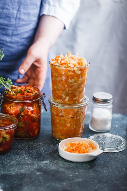 Fermented preserved vegetarian food concept. Cabbage kimchi, sauerkraut sour glass jars over the rustic kitchen table. (Shutterstock)